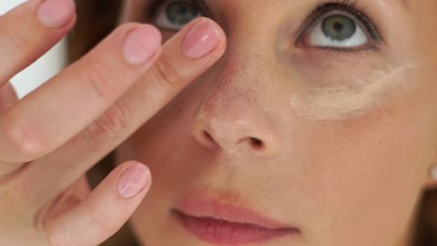 Makeup artist applying concealer cream on skin around eyes. Close up make up woman in professional beauty studio. Visagiste doing makeup face for young woman