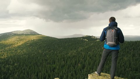 Raining In Mountains. Person Hiker Standing On Mountain Top Enjoying Rainy Weather And Storm Clouds. Hiking - hiker man on trek with backpack living healthy active lifestyle. Hike in mountain nature 