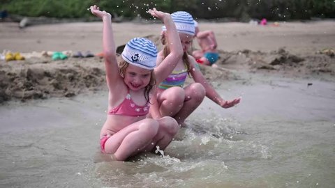 two girls splashing water on the beach. Twins pour water on a hot summer day, laughter and good mood of children