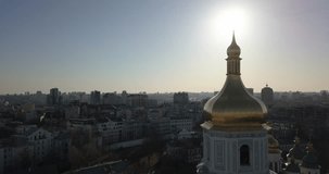 A bird's eye view, panoramic video from the drone in 4K to the golden dome of the bell tower of Saint Sophia's Cathedral in the city of Kiev, Ukraine against a bright sun.