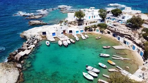 Aerial drone bird's eye view video of picturesque small fishing harbour of Mandrakia with boat houses called syrmata and fishing boats docked on turquoise clear waters, Milos island, Cyclades, Greece