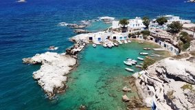 Aerial drone bird's eye view video of picturesque small fishing harbor of Mandrakia with boat houses called syrmata and fishing boats docked on turquoise clear waters, Milos island, Cyclades, Greece