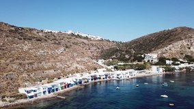 Aerial drone bird's eye view video of picturesque and colourful fishing village of Klima with traditional character and uphill village of Plaka at the background, Milos island, Cyclades, Greece