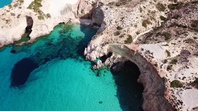 Aerial drone bird's eye view video of iconic volcanic white chalk beach and caves of Tsigrado with turquoise and sapphire clear waters, Milos island, Cyclades, Greece