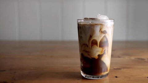 Slow motion of cream being poured into a glass of cold brew iced coffee.