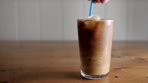 Slow motion stirring cream into a glass of cold brew iced coffee.