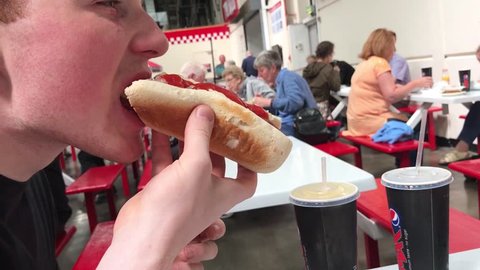 Dalkeith, Edinburgh / United Kingdom (UK) - 05 15 2018: Young man eating a Kirkland Hot Dog at Costco during the busy lunch hour