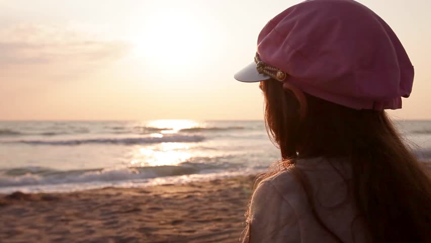 Little girl watching sunrise sea waves washing beach sand