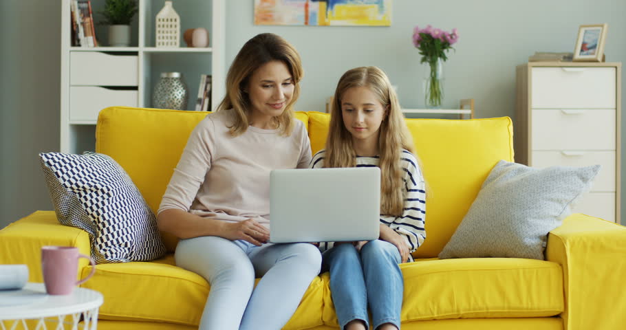 Smiled young woman showing something to her teenage daughter on the laptop computer and talking with her while they sitting in the living room. Indoors. | Shutterstock HD Video #1012831769