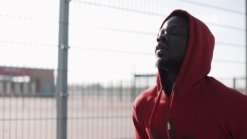 Man running at sunset in city. African American male athlete runner wearing red hoodie. Exercising outdoors fitness tracker wearable technology