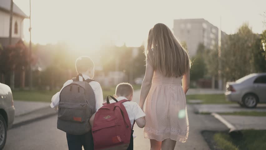 Tracking, Back view shot: Young mother goes with the school children, they tell her about successes, she smiles and praises them.  | Shutterstock HD Video #1012835285