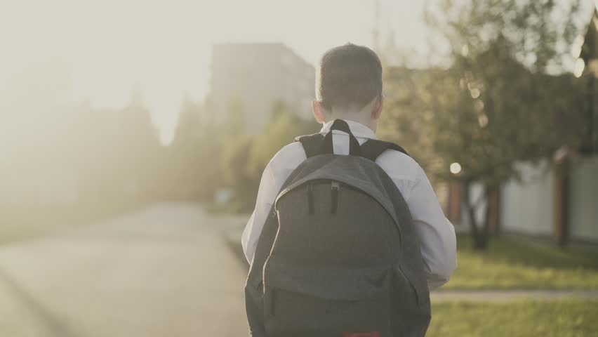 CU, Tracking, Back view: Portrait of a schoolboy, with a knapsack behind his back, in school uniform. He goes on the road from school and counts on his fingers, he thinks.  Royalty-Free Stock Footage #1012835294