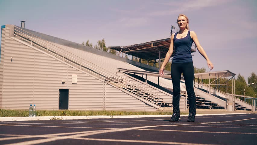 Young cute girl, sporty physique, at the stadium. She does the warm-up of the muscles, before training. 