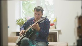 Male musician playing acoustic guitar. man playing acoustic guitar slow motion video. in the room sits on the couch. man lifestyle and guitar concept
