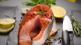 Salmon. Raw Trout Red Fish Steak with Herbs and Lemon and olive oil rotated on slate. Cooking Salmon, sea food. Healthy eating concept. Slow motion 4K UHD video