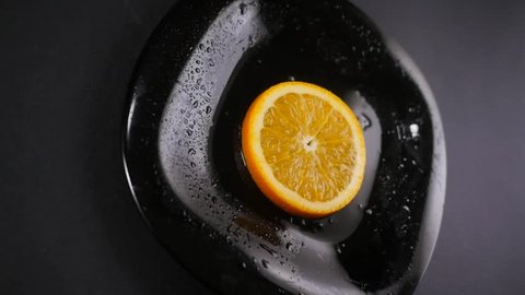 Close-up of an orange slice on a black plate with water drops : vidéo de stock
