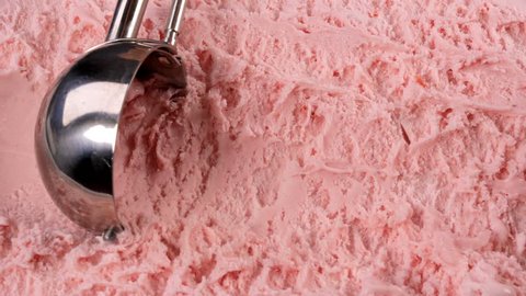 Strawberry ice cream scooped out of container with a utensil. Closeup 4k