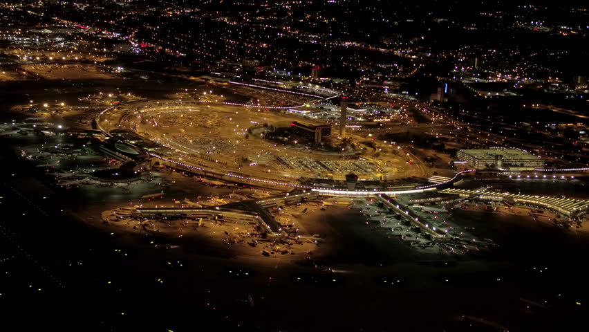 AERIAL HELI SHOT: Flying above the runway, control tower, terminal building and jet airplanes parked on apron on Newark Liberty International Airport, New Jersey lit up with lights at night.