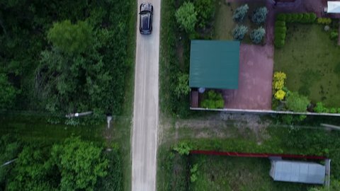 4k. Cinematic aerial footage. The village road. The car rides along the road between trees and houses and fields