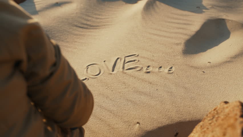 A girl in the sand draws the word 