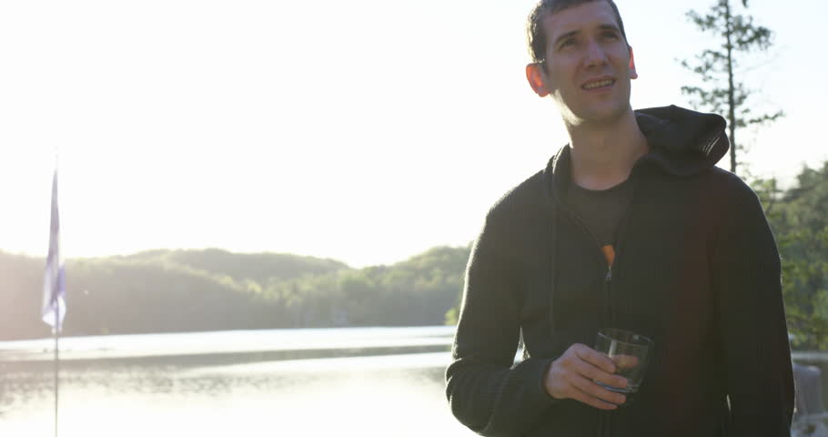 Young 20s man enjoying alcholic drink at cottage- summer time - sunset lens flare