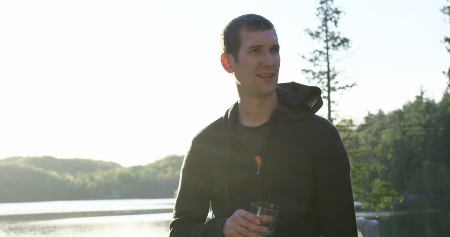 Young 20s man enjoying alcholic drink at cottage- looks up to sky on 4th of july
