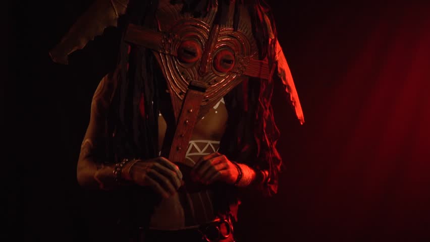 Black man in a wooden mask and white body art with ritual ornaments, conjures