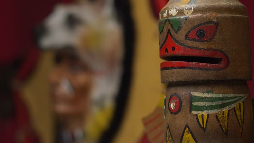 Focus pull between a native american totem and the figure of a chief wearing a wolf ornament.