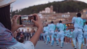 Beautiful Hispanic Woman shooting video with smartphone to folkloric dancers in Cusco, Peru