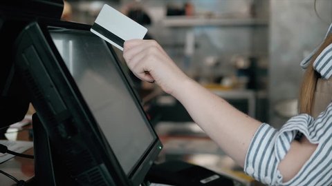 Side view of young bartender using modern cash register at bar counter