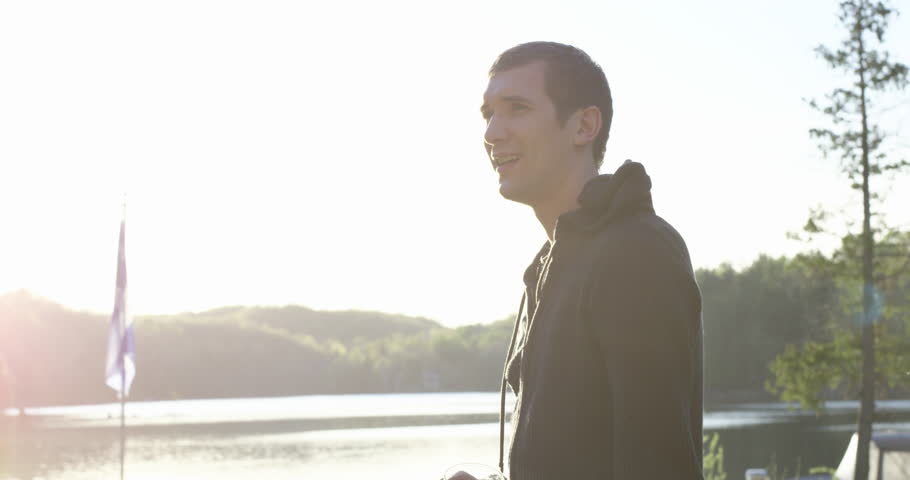 Young 20s man enjoying alcholic drink at cottage- smiles towards camera