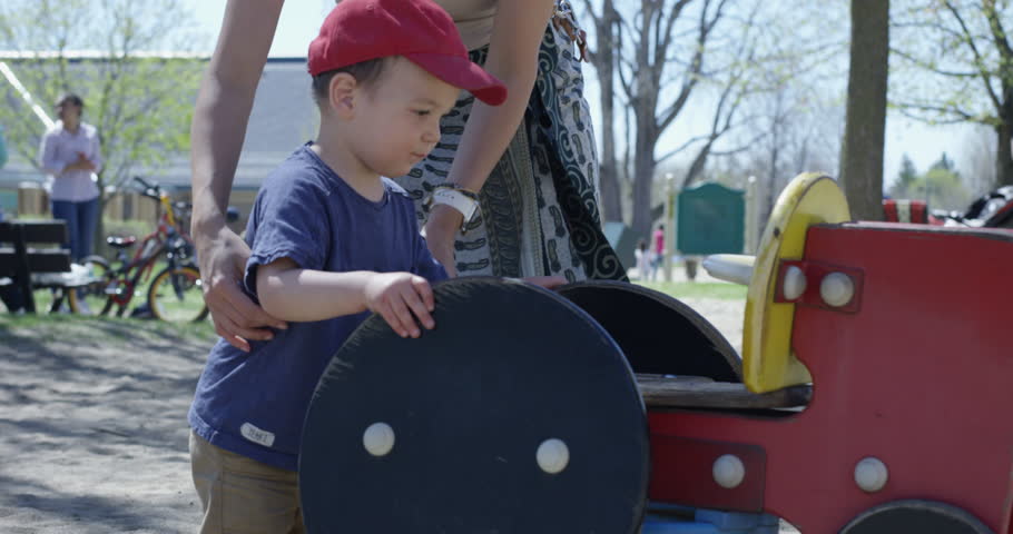 Mother puts toddler son onto toy tractor at park - close up