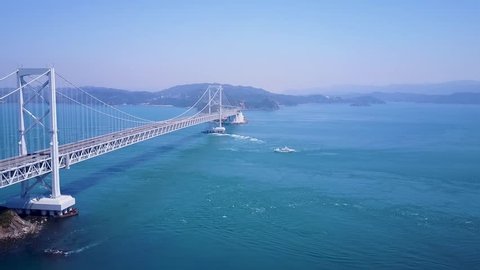 Aerial establishing shot of Great Naruto bridge in Tokushima Japan, whirlpool viewing boats below.