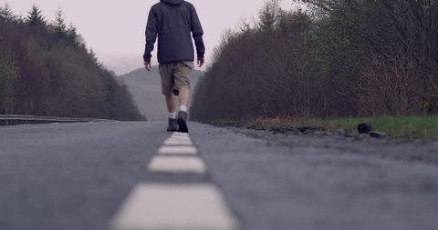 4K Hiker mans feet in walking booting waling along long empty road in the Scottish Highlands. 