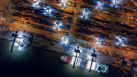 Aerial view drone time-lapse or hyper-lapse over industrial port in Bangkok Thailand with many container vessel ship and big crane working at night.