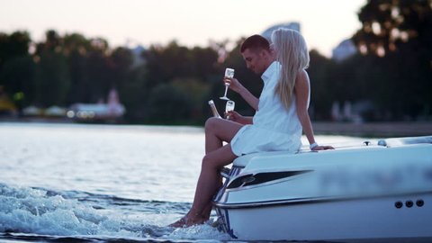 Beautiful young couple drinking champagne on floating boat. Love story concept. Luxury outdoors vacation on powerboat. Romantic date on river in evening. Love couple relaxing on floating yacht