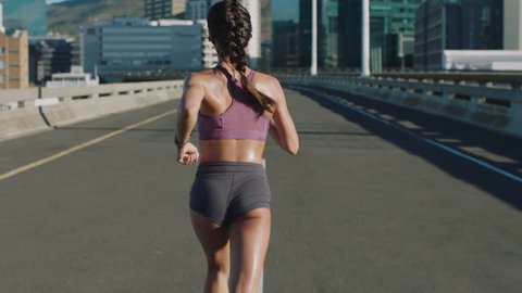 attractive young woman athlete running in city jogging exercising enjoying healthy fitness lifestyle female runner on sunny urban road rear view