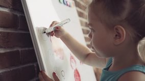 Small little girl draws picture with marker on whiteboard. Closeup FullHD video.