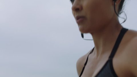 close up fit athlete woman running exercising cardio challenge intense endurance training on cloudy seaside beach healthy fitness lifestyle