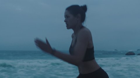 fit young woman athlete sprinting on beach running intense workout resting tired tough determined female jogging in stormy ocean seaside wearing fitness tracker