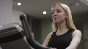 blonde girl turns the pedals on an exercise bike and enjoy the train in new gym