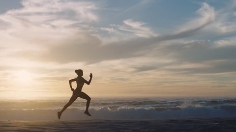 woman athlete silhouette running on beach sprinting waves crashing on seaside morning background slow motion