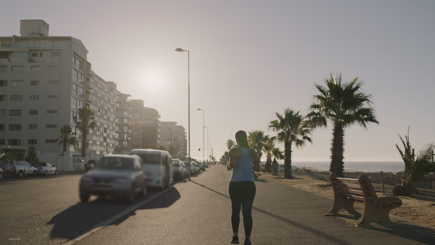 overweight woman running exercising fitness lifestyle training outdoors on early morning urban seaside background rear view slow motion