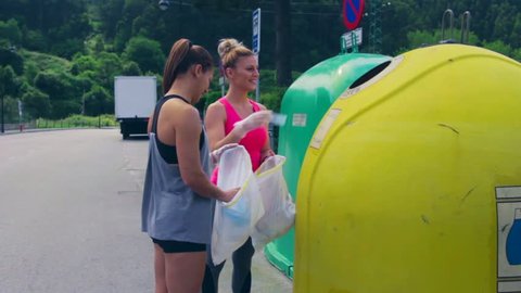 Two girls throwing garbage to recycling dumpster after plogging
