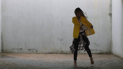 close up young happy street dancer woman dancing performing freestyle hip hop moves enjoying modern dance expression practicing in grungy warehouse wearing yellow jacket