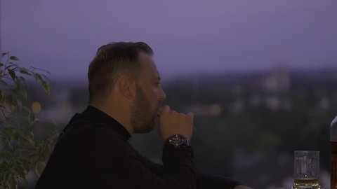 A man lights a new cigar against the background of the city in the evening.