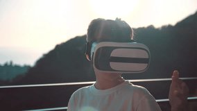 Happy boy at sunset, wearing virtual reality glasses, playing video games Cheerful smiling, looking in VR glasses and hand gesture.