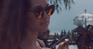 Closeup portrait of young female tourist enjoys her holiday at Ulun Danu Batur temple on the island of Bali, Indonesia - video in slow motion