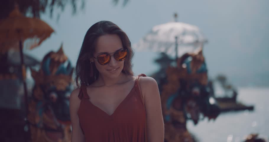 Closeup portrait of young female tourist enjoys her holiday at Ulun Danu Batur temple on the island of Bali, Indonesia - video in slow motion