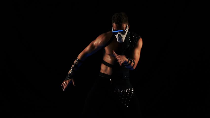 Man in a mask of a skull and glasses dance on black background